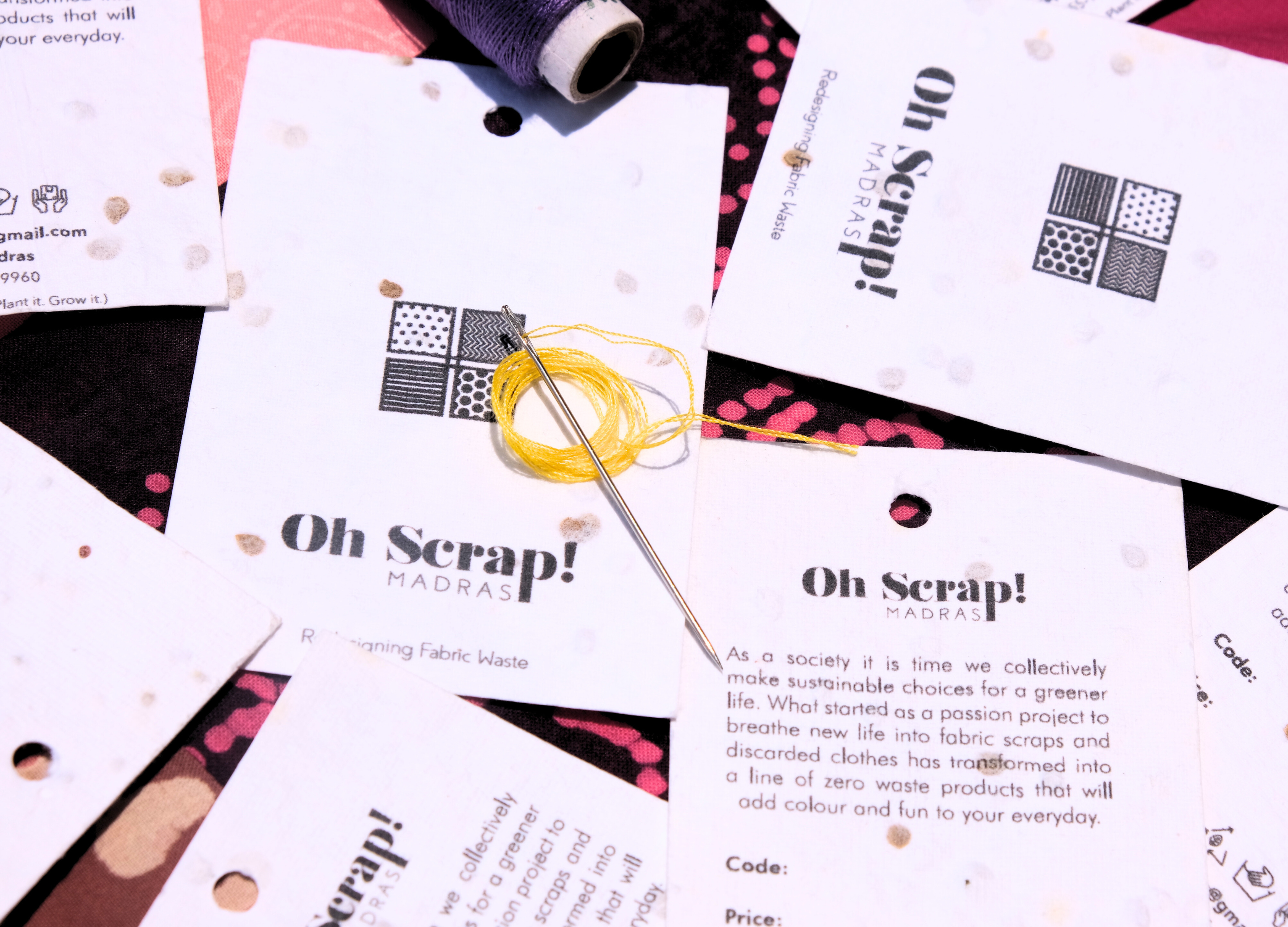 A creative arrangement of 'Oh Scrap! Madras' tags arranged on a patchwork fabric, with a needle and thread placed over it. This captivating banner represents our journey and story, a beautiful blend of memories and experiences that have shaped who we are today. Discover the heartwarming tale behind our brand on the 'Our Story' page
